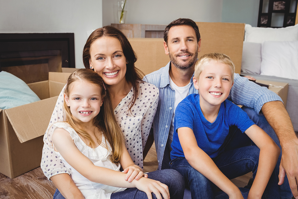 Portrait of smiling family with cardboard moving boxes in their new house after being reviewed by our home inspectors